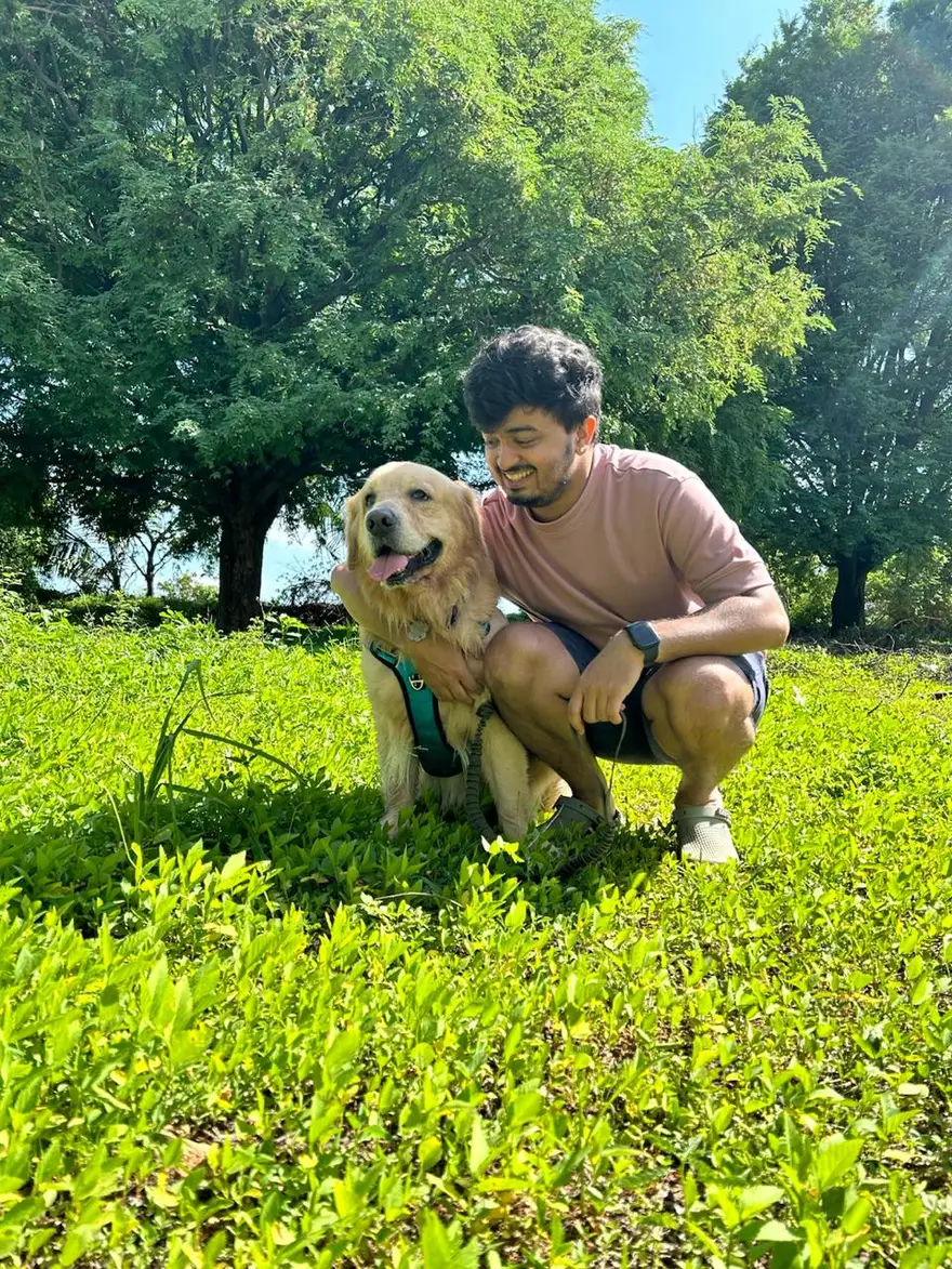 Gokul sitting with a golden retriever in a park